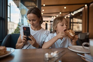 Mother and son having lunch in sidewalk restaurant.Mom and son eat a croissant in a cafe.Woman photographing food. 