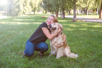 woman hugs her retriever in the park outdoors.