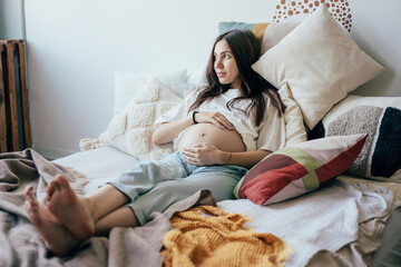 Relaxed young pregnant woman lying on the bed in the apartment. The pregnant woman gently touches her belly. Happy motherhood, health care. Waiting for the birth of a baby.