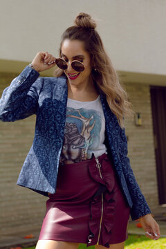 Woman in mini skirt and denim jacket with sunglasses standing outdoor