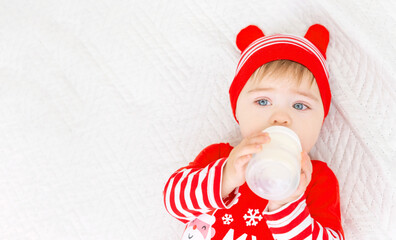 Little Caucasian baby boy wearing Christmas suit eating milk from bottle. First Christmas. Top view. White gray background. Banner, free space, copy space.
