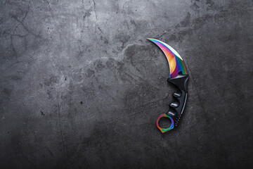 Kerambit dagger with a rainbow-colored blade on a dark textured background.