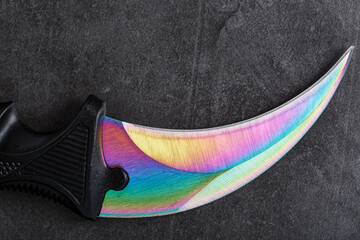 The curved sharp blade of the Kerambit Dagger is a gradient rainbow color on a dark background.