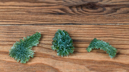 Three green raw moldavite gemstones on brown wood background. Set of beautiful mysterious glass...