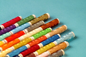 on a blue background lie diagonally spools of multi-colored thread in the lower left corner