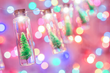 Merry Christmas and happy new year. Hanging small Christmas tree in glass jar on pine branches Christmas tree garland and ornaments over abstract bokeh
