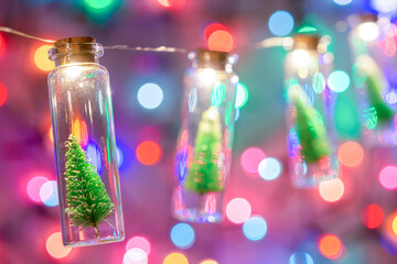 Merry Christmas and happy new year. Hanging small Christmas tree in glass jar on pine branches Christmas tree garland and ornaments over abstract bokeh