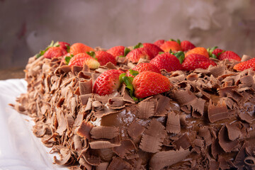 Chocolate cake, a beautiful chocolate cake with strawberries on a white shape on rustic wood, abstract background, selective focus.