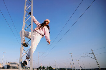 Rebellious teenage girl climbing on the metal construction at the train station.