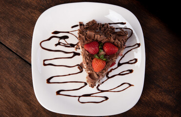 Chocolate cake, a tasty slice of chocolate cake with strawberries on a white plate on rustic wood, abstract background, Top view.