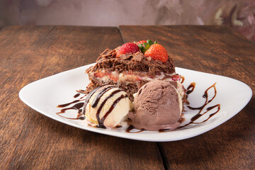 Chocolate cake, a tasty slice of chocolate cake with strawberries and ice cream balls on a white plate on rustic wood, abstract background, selective focus.
