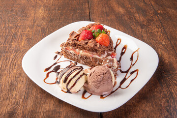 Chocolate cake, a tasty slice of chocolate cake with strawberries and ice cream balls on a white plate on rustic wood, abstract background, selective focus.