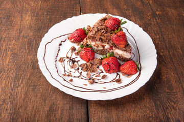 Chocolate cake, a tasty slice of chocolate cake with strawberries on a white plate on rustic wood, abstract background, selective focus.