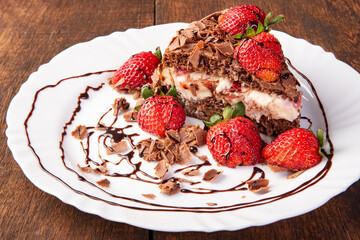 Chocolate cake, a tasty slice of chocolate cake with strawberries on a white plate on rustic wood, abstract background, selective focus.