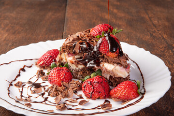 Chocolate cake, a tasty slice of chocolate cake with strawberries on a white plate on rustic wood, abstract background, selective focus.