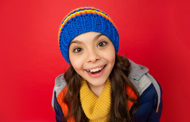 happy teen girl in knitted winter hat and down coat on red background, face