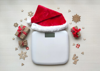 Electronic scales with Santa hat and Christmas decoration on white wooden background.