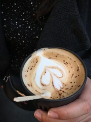 Coffee art. Detail of a girl's hand holding a coffee to take away. Latte with a drawing of a leaf. Latte art