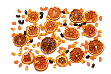 Flat lay pattern of dried orange slices, candy corn, and black jelly beans on a white background.