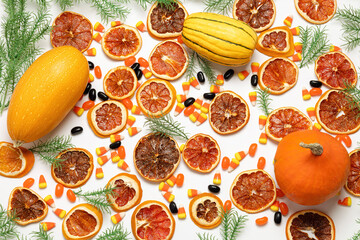 Flat lay arrangement of pumpkin, squash, dried orange slices, candy corn, jelly beans, and evergreen boughs on a white background.