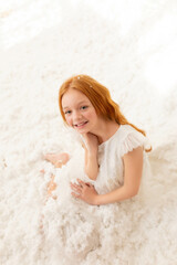 red-haired girl in an artificial snowy forest in a white dress