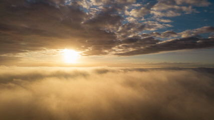 Fototapeta na wymiar Aerial View. Flying in fog, fly in mist over the early morning clouds in the rising sun. Aerial camera shot. Flight above the clouds towards the sun with the mist clouds floating by. Misty weather