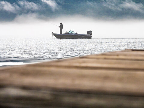 Early morning fisherman on calm lake with rolling clouds and fog