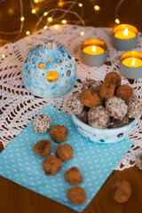 Homemade chocolate candy truffles sprinkling with cocoa, coconut chips and cookie crumbs on the table laid for Christmas or New Year with blue candlesticks and garland