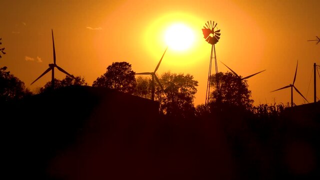 Very good shot contrasts modern wind power with traditional windmill at sunrise or sunset.