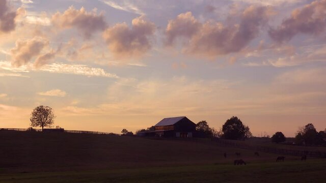 Clouds drift above a beautiful barn and horses grazing in rural Kentucky.