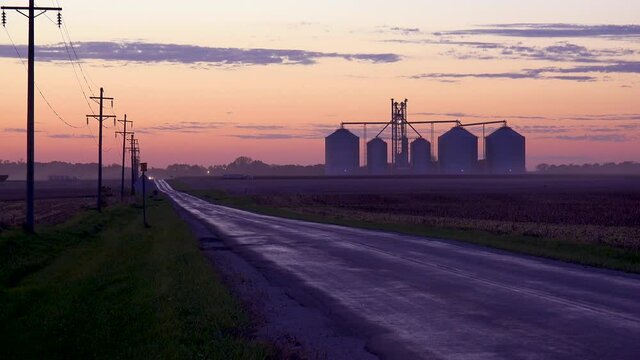 Grain silos on a large commercial farm along a country road at dusk in the Midwest.