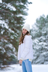 Obraz premium Close up portrait of happy girl in sweater and a knitted hat enjoying winter moments, having fun on a snowy morning on a blurred background of wood