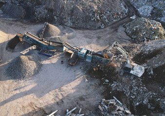 Excavator at landfill the load concrete waste in a mobile jaw crusher machine. Disposal of...
