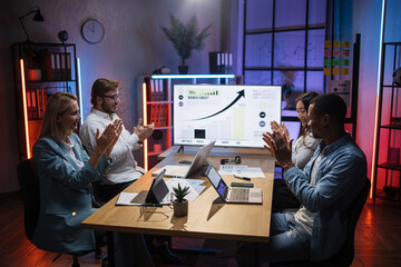 Multi ethnic male and female managers in formal clothes applauding together while sitting at office. Competent financiers with modern gadgets on table smiling after successful meeting
