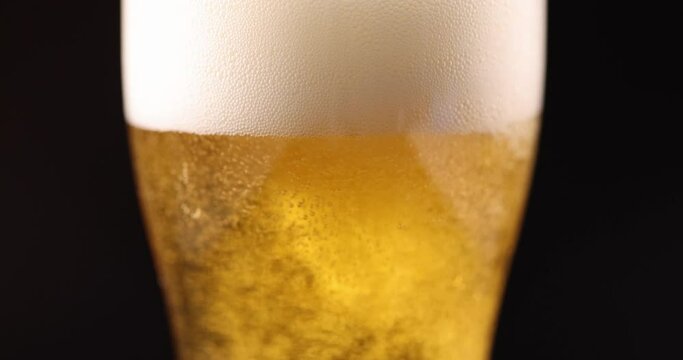 Golden beer pouring into glass with foam and many gas bubbles closeup 4k movie slow motion