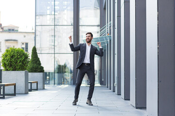 Cheerful happy business man dancing walk the city street background a modern office building outside, outdoors Funny successful businessman in suit celebtes victory