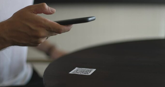 Close-up of smartphone in male hands tapping on screen. Man scanning QR code on table in restaurant or cafe. Online menu for clients. Convenience, contactless concept.
