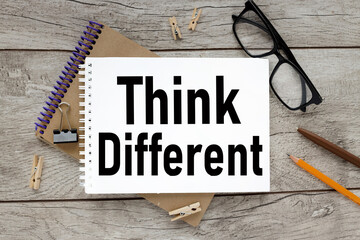 THINK DIFFERENT. text on white paper. the inscription on the notebook. business concept. notepad on a wooden background. glasses, pen, pencil