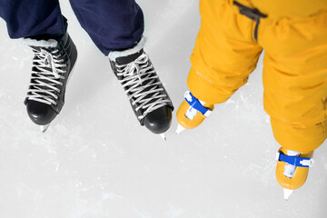 Close-up of the skates of a child and a man on an ice rink. Ice skating lessons at a hockey school. Skating shoes.  Background with a place to copy text.