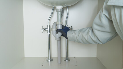 洗面台の下の配管を修理する作業員。