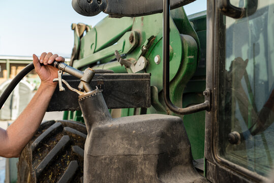 Close up view of a male farmer filling the fuel of his tractor while working on a farm. Agriculture and farming concept.