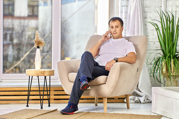 Obraz premium Mature man with phone near his ear sits in chair in living room.
