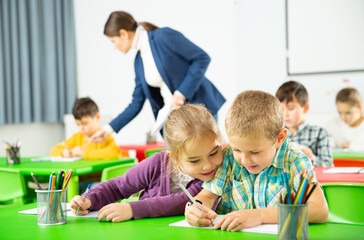 Fototapeta premium Portrait of happy schoolchildren sitting in classroom and chatting during lesson