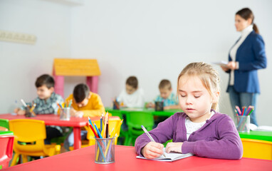 Cute preteen girl studying in classroom on background with classmates and teacher. High quality photo