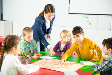 Teacher and happy children sitting at table with board game and dice in school. High quality photo