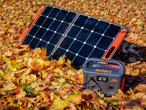 Fort Collins, CO, USA - November 4, 2021: Jackery Explorer 500, 518Wh lithium Portable Power Station, is being charged by a solar panel in a field covered by colorful dry leaves.
