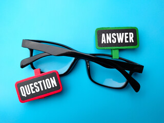 Glasses and colored wooden board with text QUESTION ANSWER on blue background.