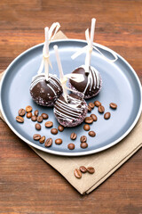 Delicious Chocolate cake pops decorated white sprinkles on plate with coffee beans on napkin, wooden background, pastry, desserts on stick with tape. Tasty food