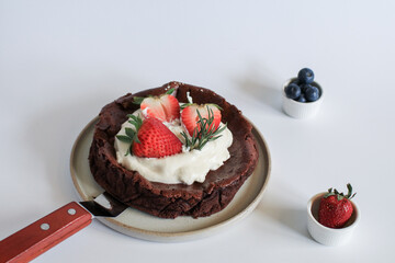 Flourless chocolate cake with whipping cream, strawberry and blueberry on white background. Homemade cake concept.