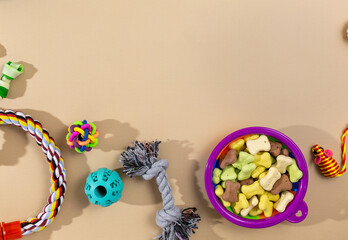 Different multicolored pet care accessories: bowl, bones, balls, snacks, mouse on beige background. Rubber and textile accessories for dogs and cats. Top view, flat lay.	